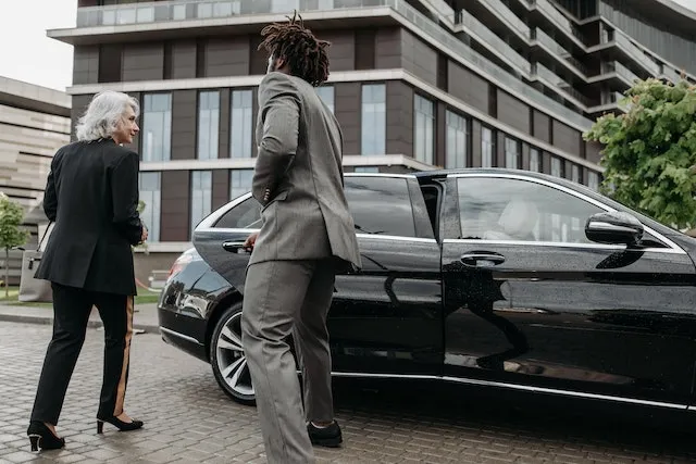 A chauffeur opening the rear door of a luxury black car for a businesswoman, representing a premium chauffeured transportation service.